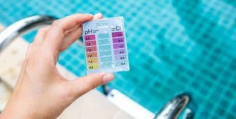 person holding a pH and chlorine test in front of a pool